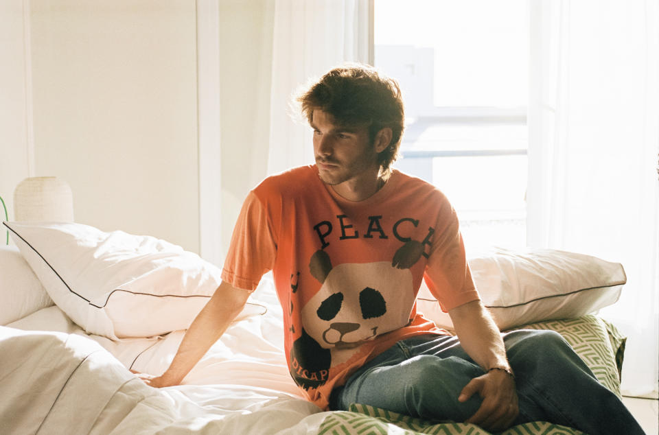 David sitting on a bed wearing a panda t-shirt with the word 'Peace' on it.