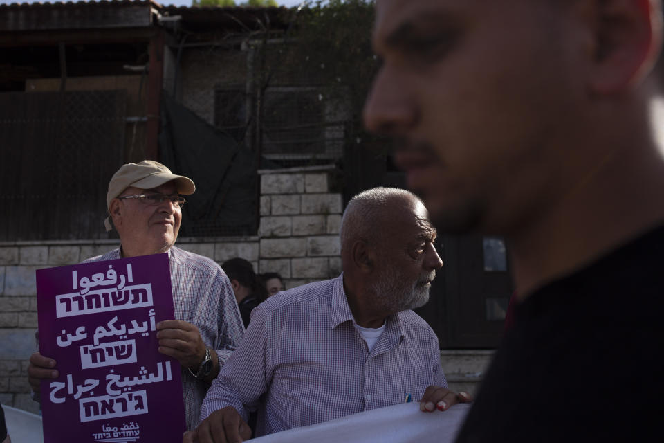 Palestinian men take part in a demonstration in the Sheikh Jarrah neighborhood of east Jerusalem, where they are among dozens of families facing imminent forcible eviction from their homes by Israeli settlers, Friday, May 28, 2021. The placard in Arabic and Hebrew expresses solidarity with Sheikh Jarrah. (AP Photo/Maya Alleruzzo)