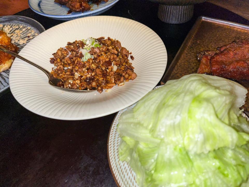 A white bowl with ground duck and green onions sits next to a plate stacked with lettuce leaves