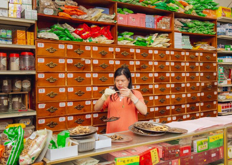 Los Angeles, CA- March 4: Shop clerk, Angela He, using the traditional copper weighted herb scale for dispensing herbs at Tian Xiang Chinese herbal medicine clinic on Saturday March 4, 2024 in Los Angeles, CA. Jason LeCras for The LA Times.