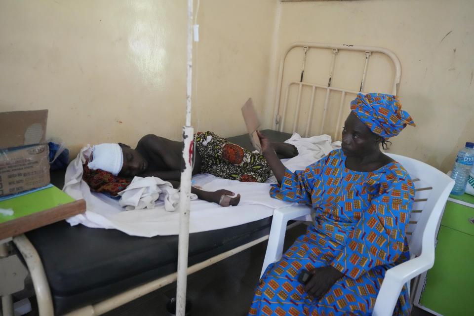 A woman fans a victim of St. Francis Catholic Church attack receiving treatment at St Louis Catholic Hospital in Owo Nigeria, Monday, June 6, 2022. Lawmakers in southwestern Nigeria say more than 50 people are feared dead after gunmen opened fire and detonated explosives at a church. Ogunmolasuyi Oluwole with the Ondo State House of Assembly said the gunmen targeted the St Francis Catholic Church in Ondo state on Sunday morning just as the worshippers gathered for the weekly Mass. (AP Photo/Sunday Alamba)