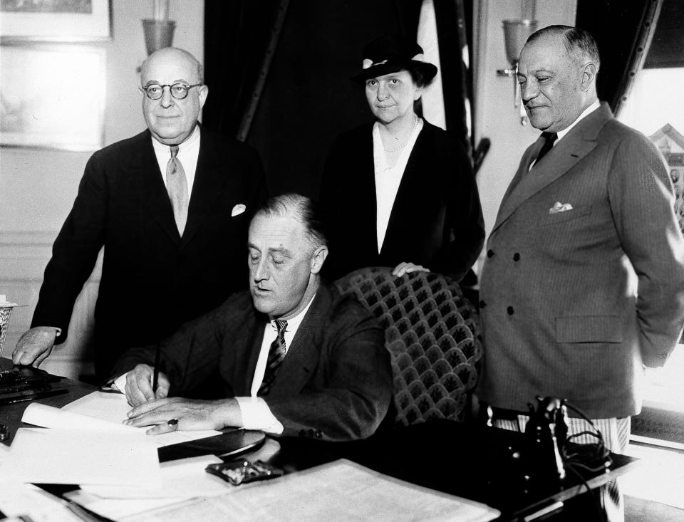 President Franklin D. Roosevelt is shown signing the Wagner Unemployment Bill, June 6, 1933, at the White House.  Standing, left to right:  Rep. Theodore A. Peyser of New York; Secretary of Labor Frances Perkins; and Sen. Robert Wagner of New York.