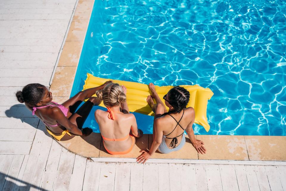 three women sitting by a pool in the sun