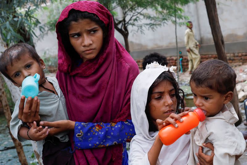 Girls, who along with their families are displaced by flooding, give water to their siblings, as they take refuge in a school, in Jacobabad