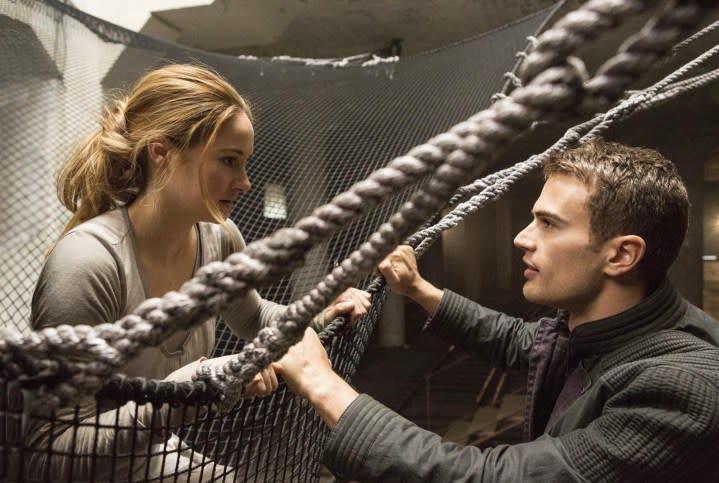 A man holds onto ropes and looks up at a girl.