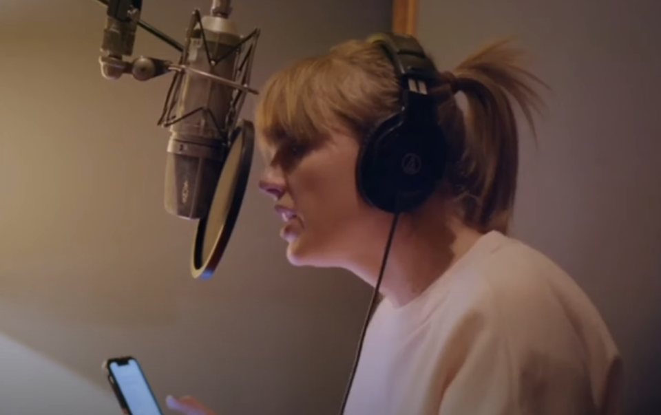 Woman in a recording studio speaking into a microphone while reading from a smartphone