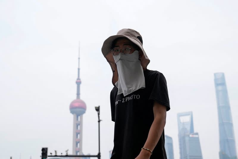 A man walks on the Bund as he shields himself from the sun with a hat and mask, on a hot day in Shanghai