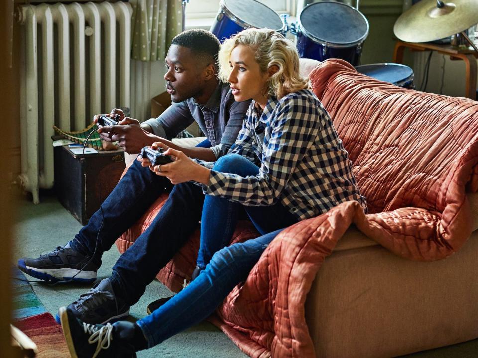 Two friends sit on an orange couch playing video games.