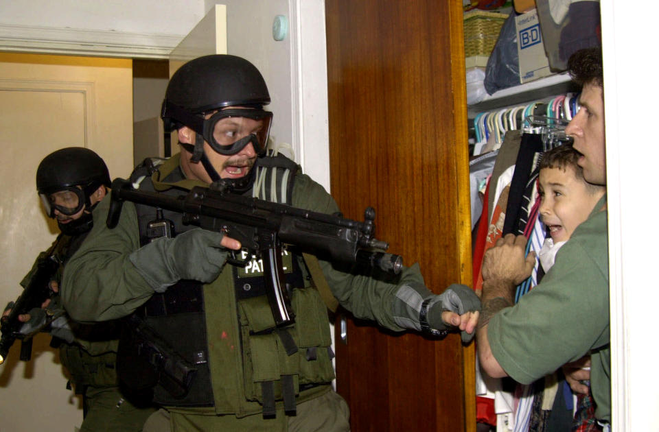 FILE- In this file photo taken April 22, 2000, in Miami, Elian Gonzalez is held in a closet by Donato Dalrymple, one of the two men who rescued the boy from the ocean, right, as government officials search the home of Lazaro Gonzalez for the young boy. The boy was eventually reunited with his father in Cuba, but the ordeal put a spotlight on bitter relations between the U.S. and Cuba. (AP Photo/Alan Diaz, File)