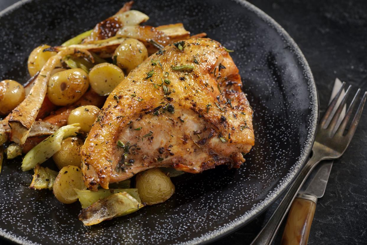 Slow cooker garlic parmesan chicken and potatoes on a black ceramic plate with fork and knife with a black background