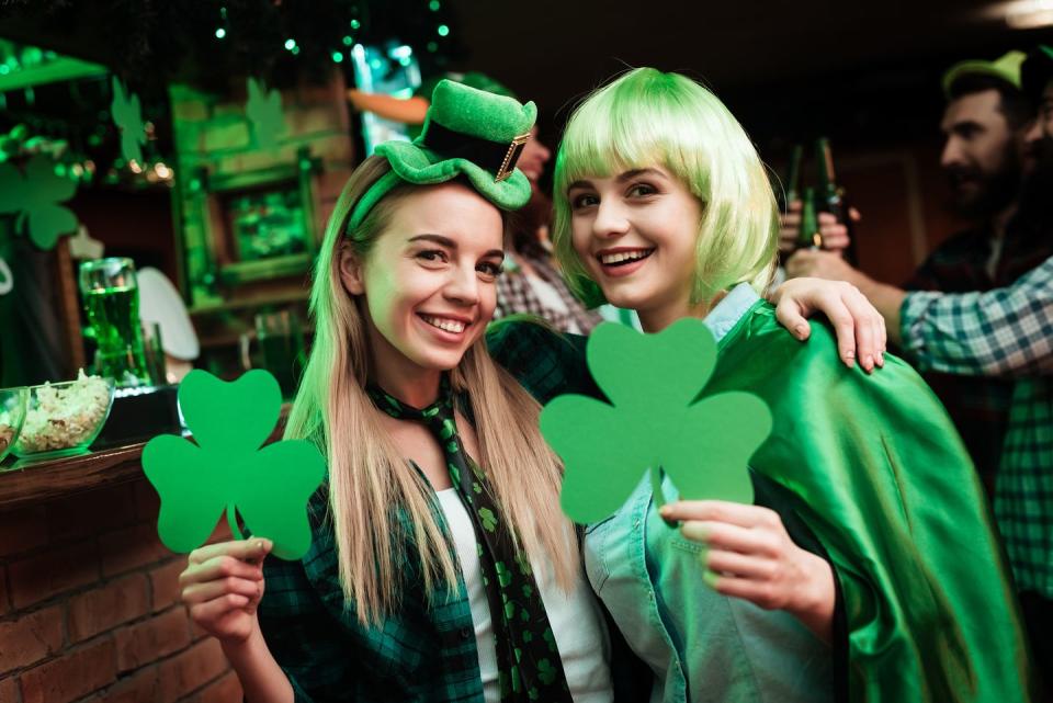 two girls in a wig and a cap are photographed in a bar they celebrate st patricks day they are having fun one girl is holding a clover