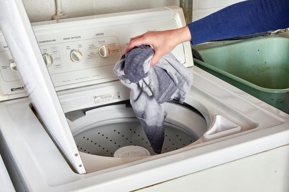 Woman puts a shirt into a top-loader washing machine.