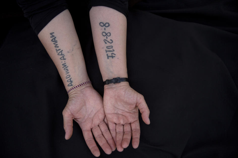 In this Thursday, Aug. 29, 2019 photo, Leila Shamo displays tattoos she made while enslaved by Islamic State militants at her home near Khanke Camp, near Dohuk, Iraq. Shamo, 34, has used her breast milk, charcoal ash and a needle to write the names of her husband, and two sons on the front of her hand and the inside of her right forearm: Kero, Aadnan, Aatman. On the inside of her left forearm, she wrote the date IS militants captured them all together: 8-8-2014. The mother of five tattooed their names and her date of capture on her skin to spite her captors and to never forget. (AP Photo/Maya Alleruzzo)