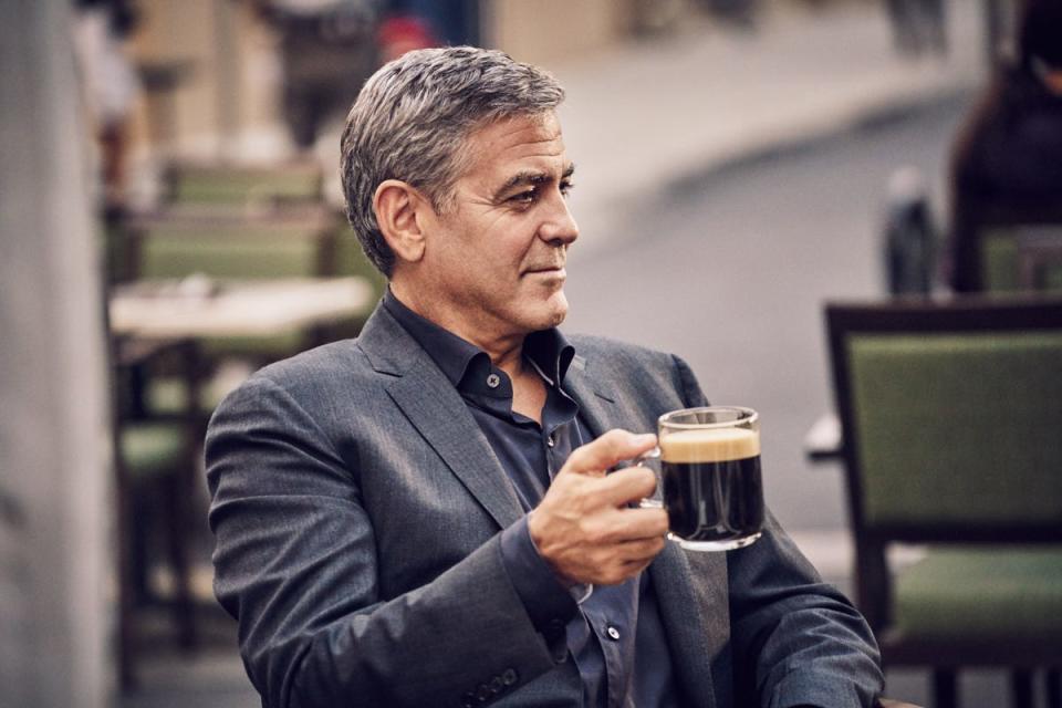 George Clooney in a gray jacket holding a coffee