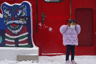 A child puts on her face mask to help protect from the coronavirus next to a lion dancer decoration at a mall in Beijing, Sunday, Jan. 23, 2022. Chinese authorities have called on the public to stay where they are during the Lunar New Year instead of traveling to their hometowns for the year's most important family holiday. (AP Photo/Andy Wong)