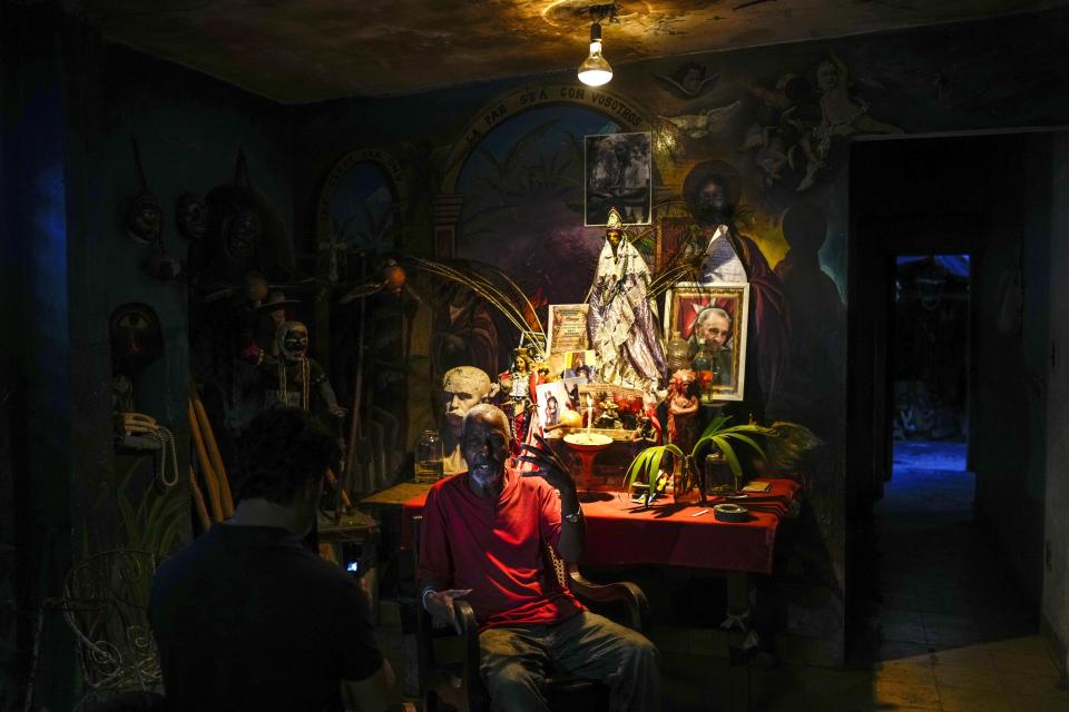 Juan González se sienta junto a un altar adornado con estatuillas de deidades de la santería afrocubana, incluida "Oshún" y una foto del fallecido líder cubano Fidel Castro, en su casa de El Cobre, Cuba, el sábado 10 de febrero de 2024. (AP Foto/Ramón Espinosa)