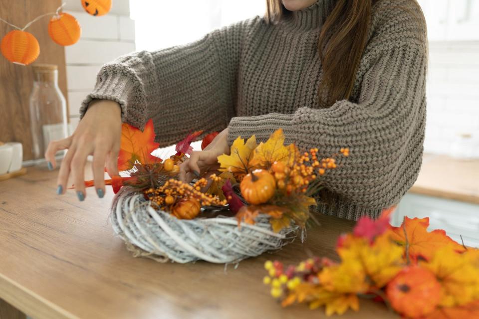 unrecognisable woman making halloween orange decorations of leaves, pumpkin, berry twigs for holidays