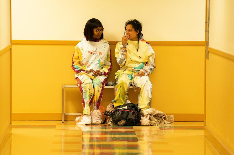 Two women, dressed in yellow, sit in a yellow hallway