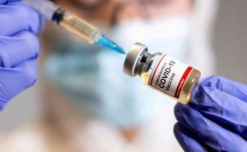 FILE PHOTO: A woman holds a medical syringe and a small bottle labeled "Coronavirus COVID-19 Vaccine