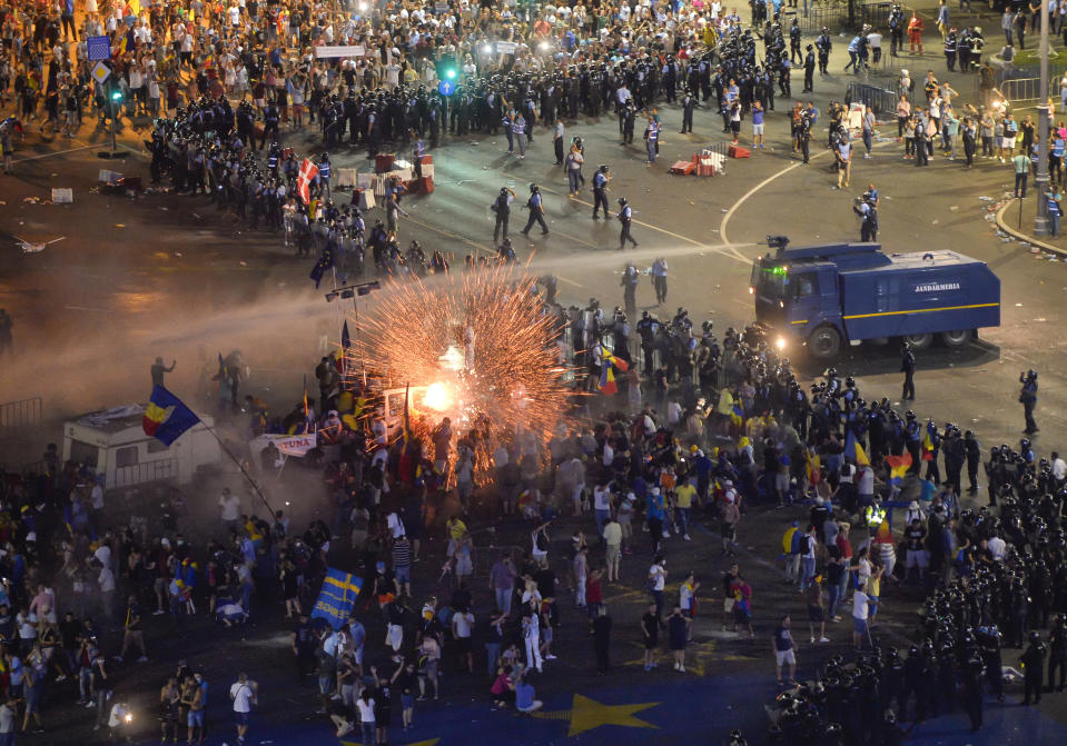 In this Friday, Aug. 10, 2018, photo, a teargas canister explodes as riot police charge using canon to clear the square during protests outside the government headquarters in Bucharest, Romania. Romanian authorities say hundreds of people including two dozen riot police have received medical treatment after an anti-government protest turned violent and two weapons were stolen from riot police officers. (AP Photo/Andreea Alexandru)
