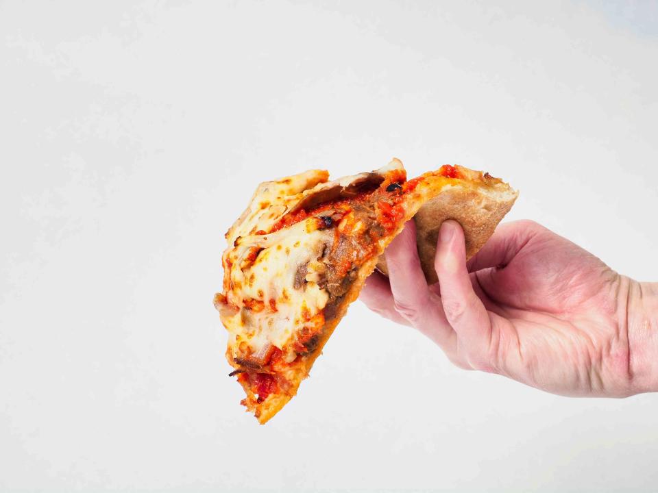 <p>A hand holding a overloaded slice of pizza folded over and about to fall on the floor. </p>