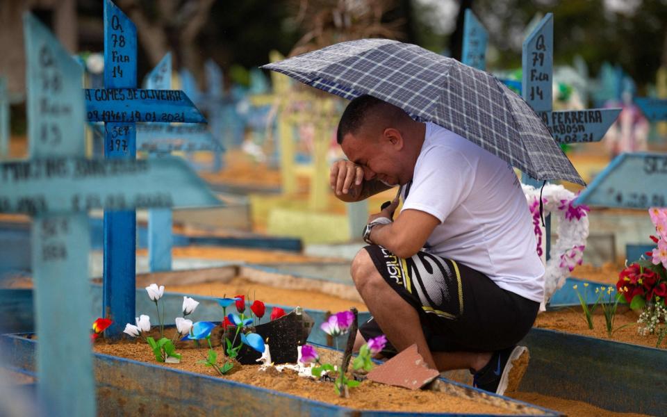 A man cries by a grave at the Nossa Senhora Aparecida cemetery in Manaus - AFP