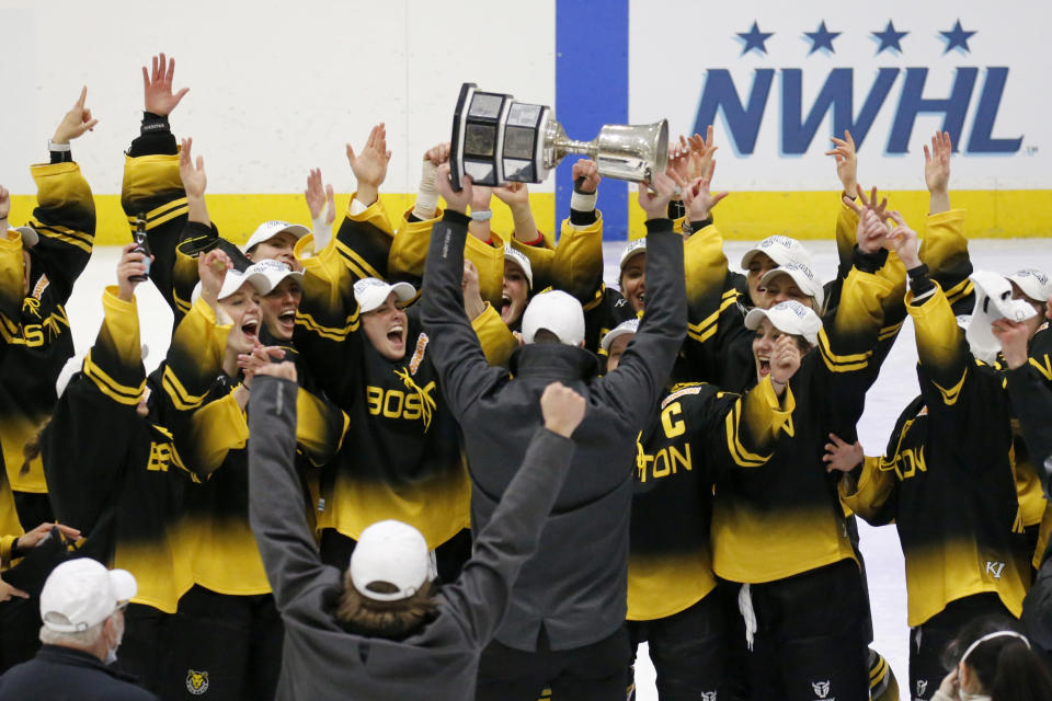 FILE - Boston Pride players cheer as coach Paul Mara hoists the NWHL Isobel Cup trophy after the team's win over the Minnesota Whitecaps in the championship hockey game in Boston, Saturday, March 27, 2021. The Premier Hockey Federation is more than doubling each teams’ salary cap to $750,000 and adding two expansion franchises next season in a bid to capitalize on the wave of attention women’s hockey traditionally enjoys following the Winter Olympics. (AP Photo/Mary Schwalm, File)