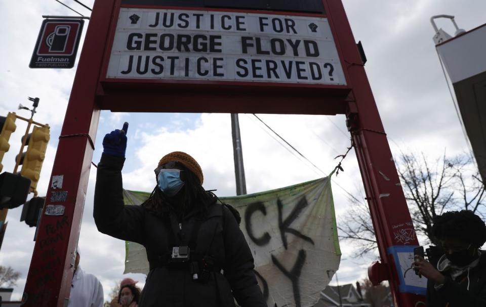 A person wearing a winter hat and jacket standing in front of a sign that reads "Justice for, George Floyd, Justice Served?"