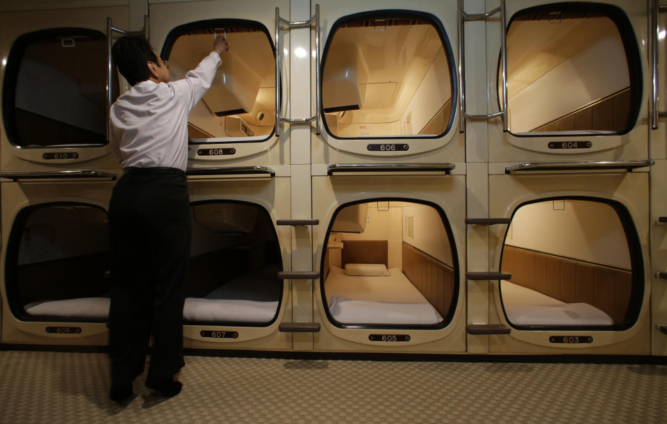 In this Monday, Oct. 29, 2012 photo, manager Akiyoshi Kaneko stands by the rooms at the Capsule & Sauna Century Shibuya in Tokyo. The capsule concept has been around for at least 30 years, starting out as lodging for businessmen working or partying late who missed the last train home and needed a cheap place to crash. But budget travelers and other folks curious about a unique lodging experience use them too. (AP Photo/Shizuo Kambayashi)