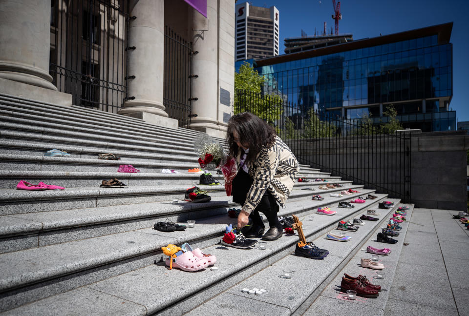 <p>Delhia Nahanee, of the Squamish Nation, places a rose on one of 215 pairs of children's shoes on the steps of the Vancouver Art Gallery as a memorial to the 215 children whose remains have been found buried at the site of a former residential school in Kamloops, in Vancouver, on Friday, May 28, 2021. Chief Rosanne Casimir of the Tk’emlups te Secwépemc First NationFirst Nation said in a news release Thursday that the remains were confirmed last weekend with the help of a ground-penetrating radar specialist. THE CANADIAN PRESS/Darryl Dyck</p> 