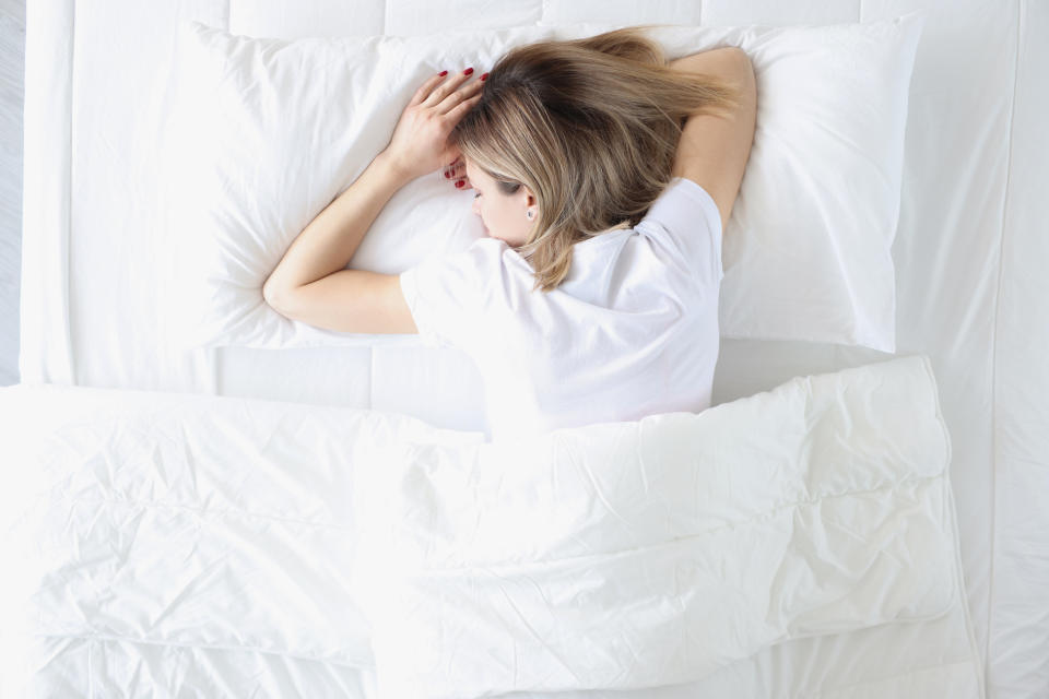 Young woman sleeping on her stomach in white bed top view. Healthy sleep concept