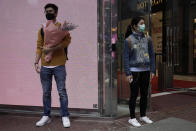 A man wearing protective face mask waits at a street corner with a bouquet on Valentine's Day in Hong Kong, Friday, Feb. 14, 2020. China on Friday reported another sharp rise in the number of people infected with a new virus, as the death toll neared 1,400. (AP Photo/Kin Cheung)