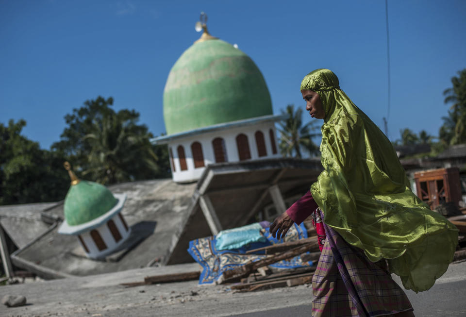 In this Saturday, Aug. 11, 2018, photo, a Muslim woman walks past a mosque collapsed during Sunday's earthquake in Gangga, Lombok Island, Indonesia. Scientists say the powerful earthquake that killed hundreds of people lifted the island it struck by as much as 25 centimeters (10 inches). (AP Photo/Fauzy Chaniago, File)