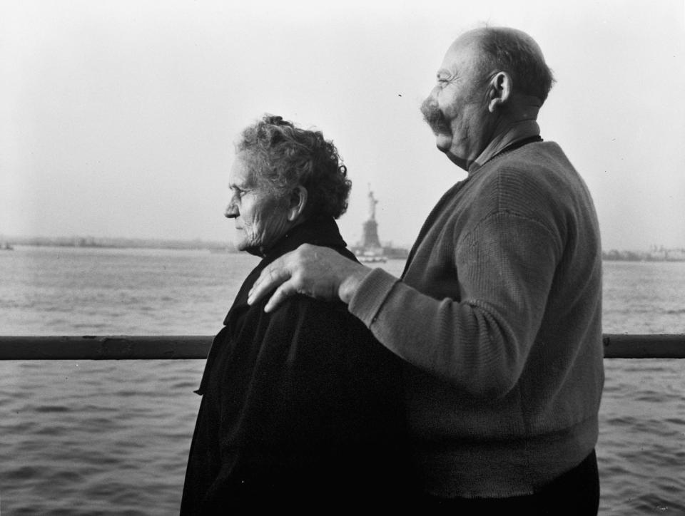 FILE - In this Oct. 28, 1956, file photo, Mr. and Mrs. Paul Roerich from Bavaria, Germany, look out from the stern of the USNS General Langfitt anchored in New York Harbor carrying over a 1,000 refugees from Europe. In the background is the Statue of Liberty. The couple planned to settle in Ohio. (AP Photo/File)