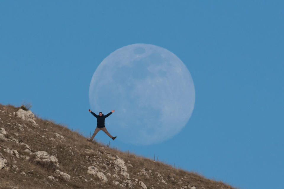 a person spreads their arms and legs wide in front of the full moon