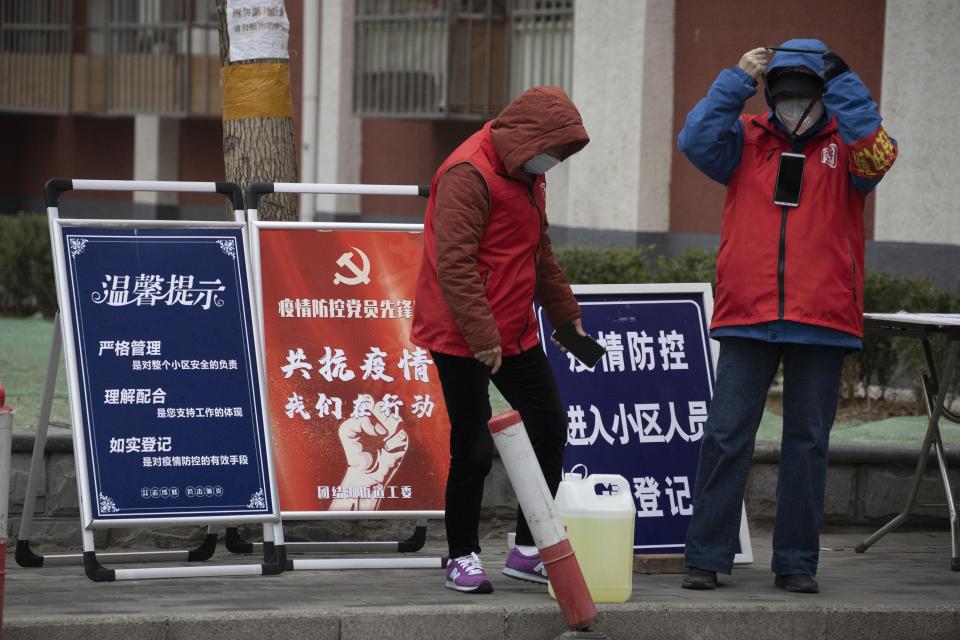 In this photo taken Sunday, March 8, 2020, community workers stand near propaganda board which reads "Outbreak Prevention and Control, Communist Party Member Pioneer station" in Beijing. As the rest of the world grapples with a burgeoning virus outbreak, China's ruling Communist Party has turned to its propaganda playbook to portray its leader as firmly in charge, leading an army of health workers in a "people's war" against the disease. (AP Photo/Ng Han Guan)