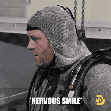 A person in a chainmail suit, with scuba gear, labeled with *Nervous Smile*, stands and smiles. The Discovery Channel logo is in the lower right corner