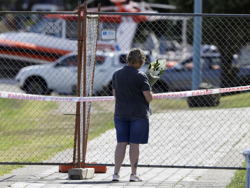 A woman places a bouquet of flowers at the fence of a restricted area on the waterfront in Whakatane, New Zealand, Tuesday, Dec. 10, 2019. A volcanic island in New Zealand erupted Monday in a tower of ash and steam while dozens of tourists were exploring the moon-like surface, killing several people and leaving many more missing. (AP Photo/Mark Baker)