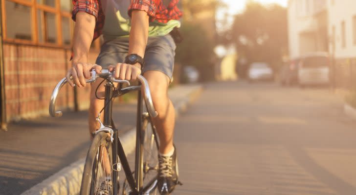A photo of a person in shorts and a flannel shirt riding a bicycle in an urban environment.