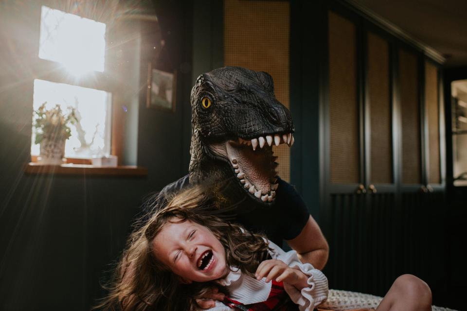 Una niña juega junto con otra persona disfrazada de dinosaurio. 