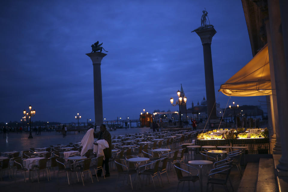 A worker removes tablecloths in an empty restaurant terrace at the St. Mark's Square in Venice, Saturday, Feb. 29, 2020. A U.S. government advisory urging Americans to reconsider travel to Italy due to the spread of a new virus is the "final blow" to the nation's tourism industry, the head of Italy's hotel federation said Saturday. Venice, which was nearing recovery in the Carnival season following a tourist lull after record flooding in November, saw bookings drop immediately after regional officials canceled the final two days of celebrations this week, unprecedented in modern times. (AP Photo/Francisco Seco)