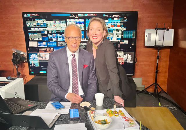 <p>NBC News</p> Lester Holt’s wife, Carol Hagen, brings him a plate of food from the party while he prepares the special report