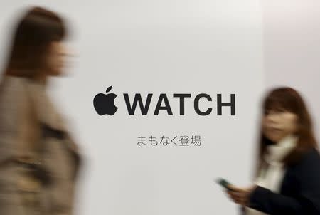 A pedestrian using her smartphone walks past an advertisement board for Apple Watch outside the Isetan department store, where an Apple Watch store will be located, in Tokyo April 9, 2015, a day before the shop opens and starts accepting reservations for the Apple Watch. REUTERS/Yuya Shino