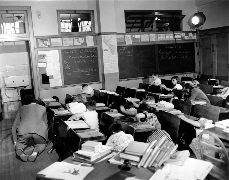 Sixth grade students crouch under or beside their desks along with their teacher, Vincent M. Bohan, left, as they act out a scene from the Federal Civil Defense administration film 