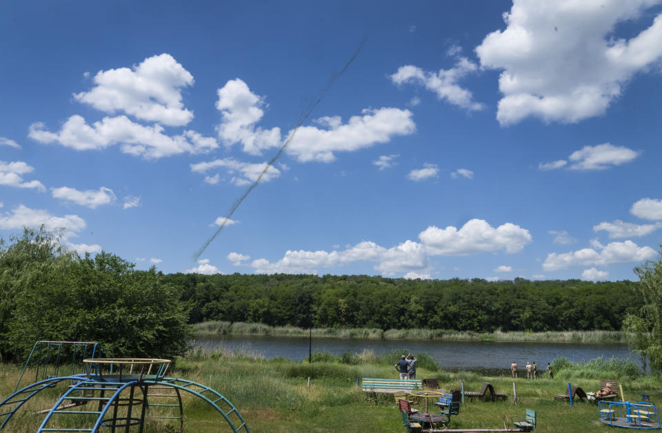 People enjoy a sunny day by the lake in a city park as a rocket trail is seen in the sky above them in Bakhmut, Donetsk region, Ukraine, Sunday, June 19, 2022. (AP Photo/Efrem Lukatsky)