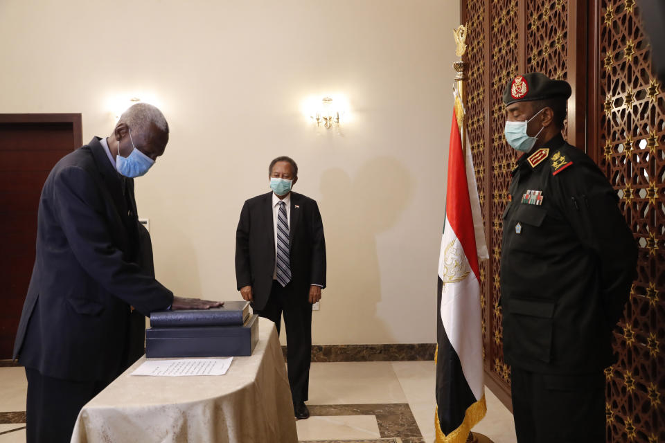 Maj. Gen. Yassin Ibrahim Yassin, left, takes the oath as Minister of Defense in front of Gen. Abdel-Fattah Burhan, head of the ruling sovereign council, right, in the presence of Prime Minister Abdalla Hamdok, center, at the Presidential Palace in Khartoum, Sudan, Tuesday, June 2, 2020. The ceremony came more than two months after the death of the former defense chief and amid tensions with neighboring Ethiopia. (AP Photo/Marwan Ali)