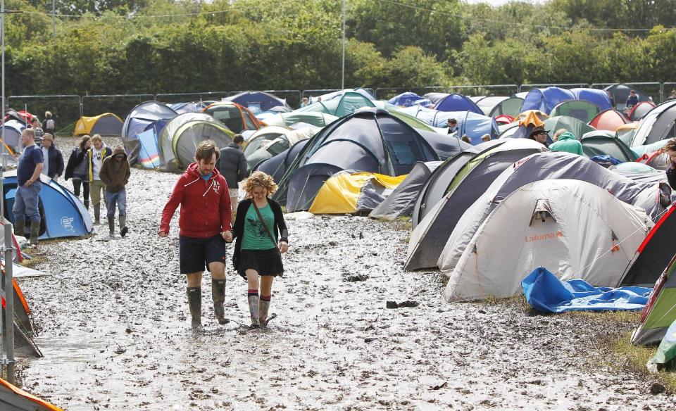 Festival goers walk through the mud at the campsite at the Isle of Wight festival on the Isle of Wight england Friday June 22, 2012. Hundreds of music fans have been stranded in their cars overnight after rainstorms caused chaos on travel routes to the Isle of Wight Festival. (AP Photo/Peter Byrne/PA) UNITED KINGDOM OUT