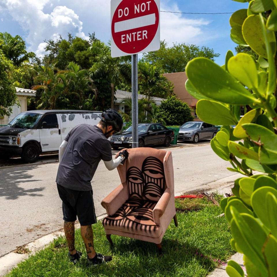 Local street artist Ahol Sniffs Glue draws on an arm chair that was left on the side of the road as trash.