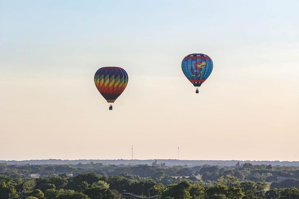 Hot-air balloons - one with a rainbow design and another sporting a Kansas Jayhawk - take flight at the kick-off start to the FireLake Fireflight Balloon Fest on Thursday, Aug. 11, 2022, in Shawnee.