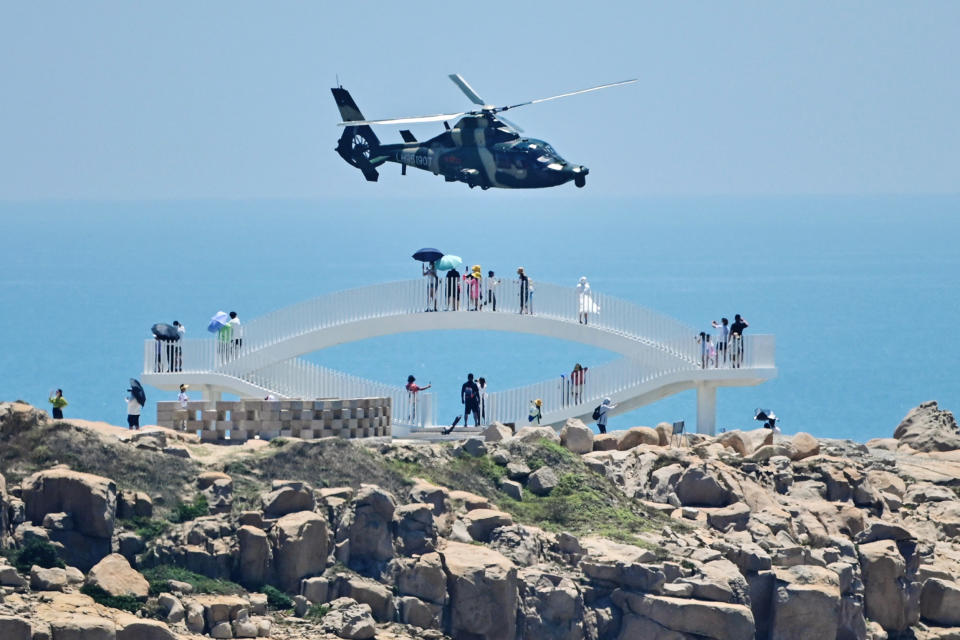 Tourists look on as a Chinese military helicopter flies past China's Pingtan Island, the closest point to Taiwan, on Aug. 4, 2022, ahead of massive military drills. (Hector Retamal / AFP via Getty Images file)